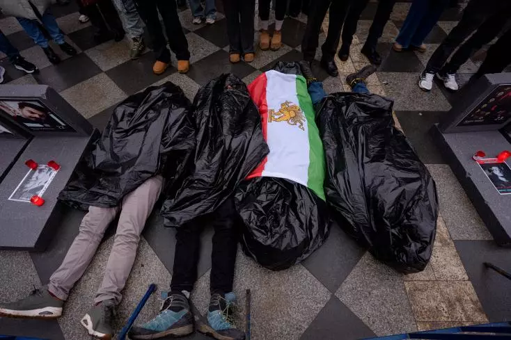 Des personnes recouvertes de sacs plastique symbolisant des victimes sont allongées sur le trottoir lors d'un rassemblement de soutien aux manifestations anti-gouvernementales en Iran, à Bucarest, Roumanie, samedi 24 janvier 2026.